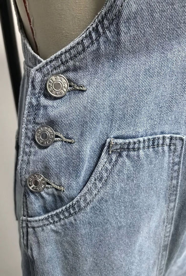 Close-up of metal side buttons and front patch pocket on women’s light blue denim overalls
