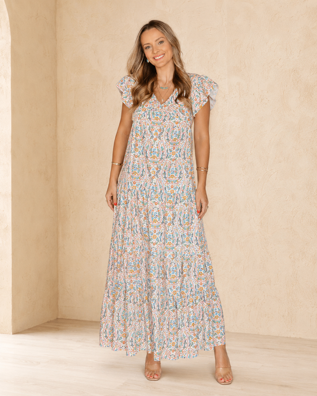 Front view of an ivory horseshoe floral tiered maxi dress with ruffle cap sleeves